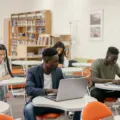 Mahasiswa sedang menggunakan laptop untuk kuliah di area perpustakaan kampus