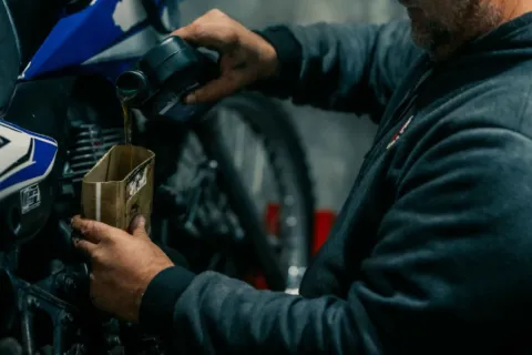 Mekanik berpengalaman sedang menuangkan cairan oli motor berkualitas ke dalam mesin motor matic untuk perawatan rutin
