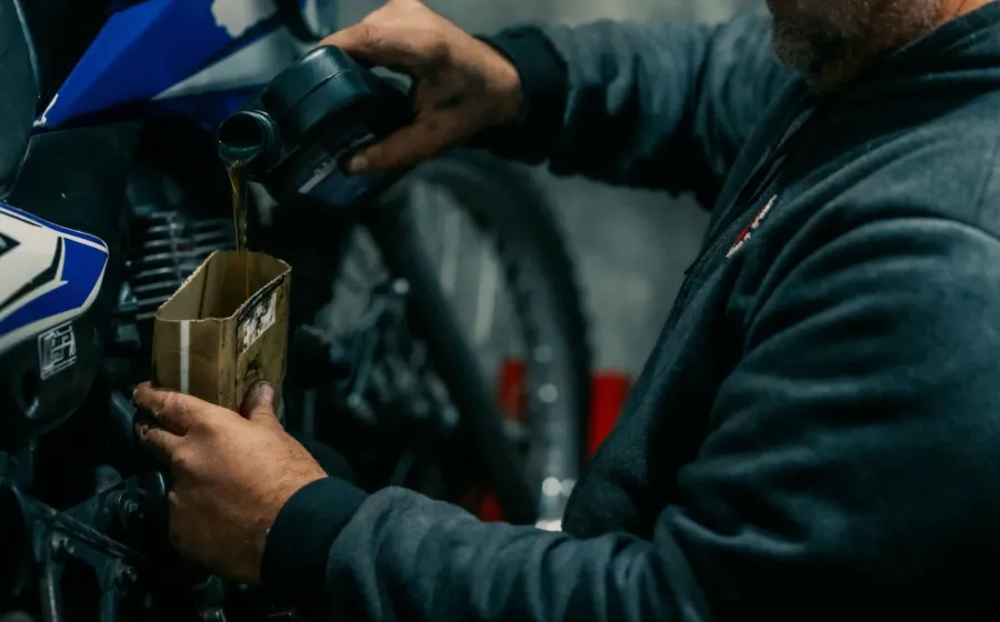 Mekanik berpengalaman sedang menuangkan cairan oli motor berkualitas ke dalam mesin motor matic untuk perawatan rutin